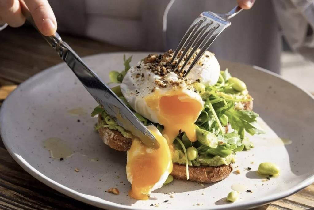 Close-up of a poached egg being cut on avocado toast .