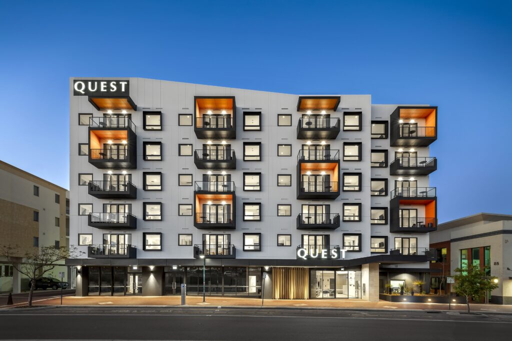 Modern Quest hotel building with black and orange balconies against a blue sky.